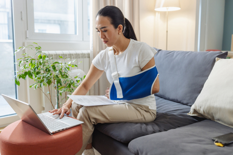 woman wearing arm sling sitting on sofa using a laptop